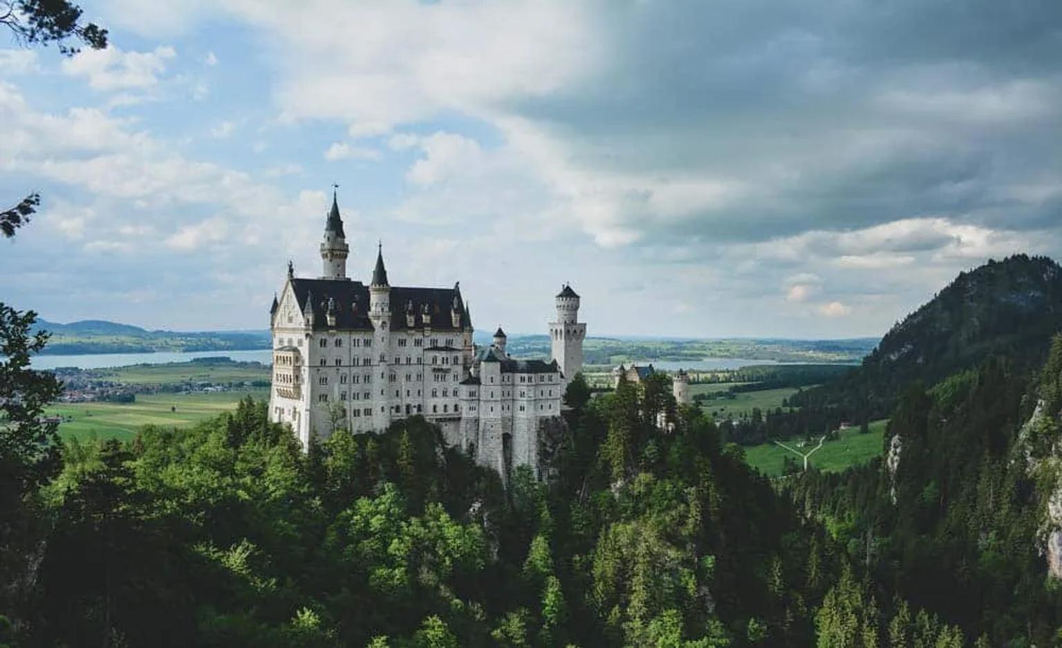 Castillo en un paisaje montañoso, rodeado de árboles y campos verdes.
