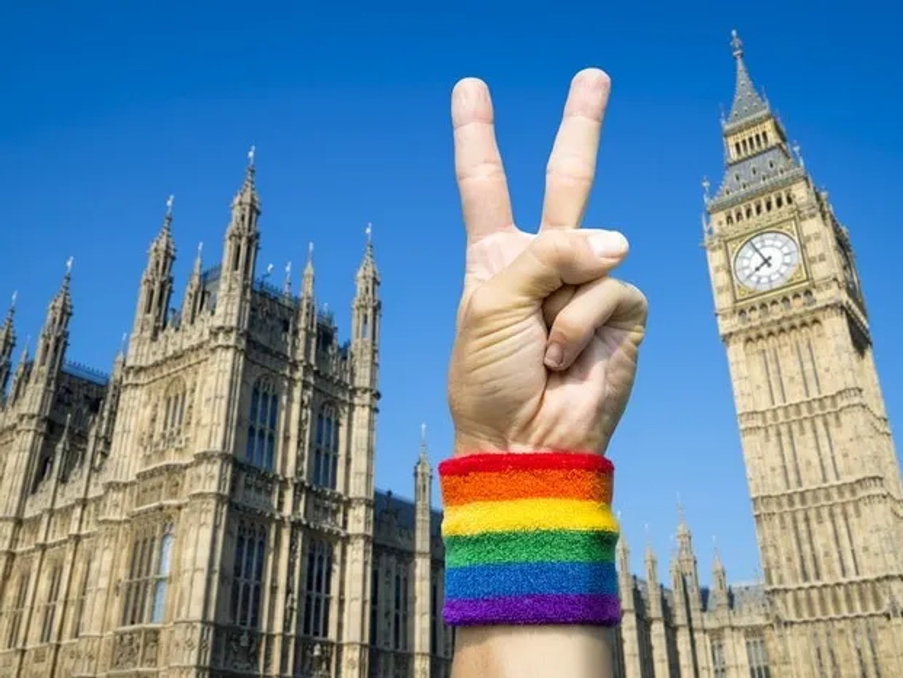 Mano con pulsera arcoíris haciendo signo de paz frente al Big Ben.