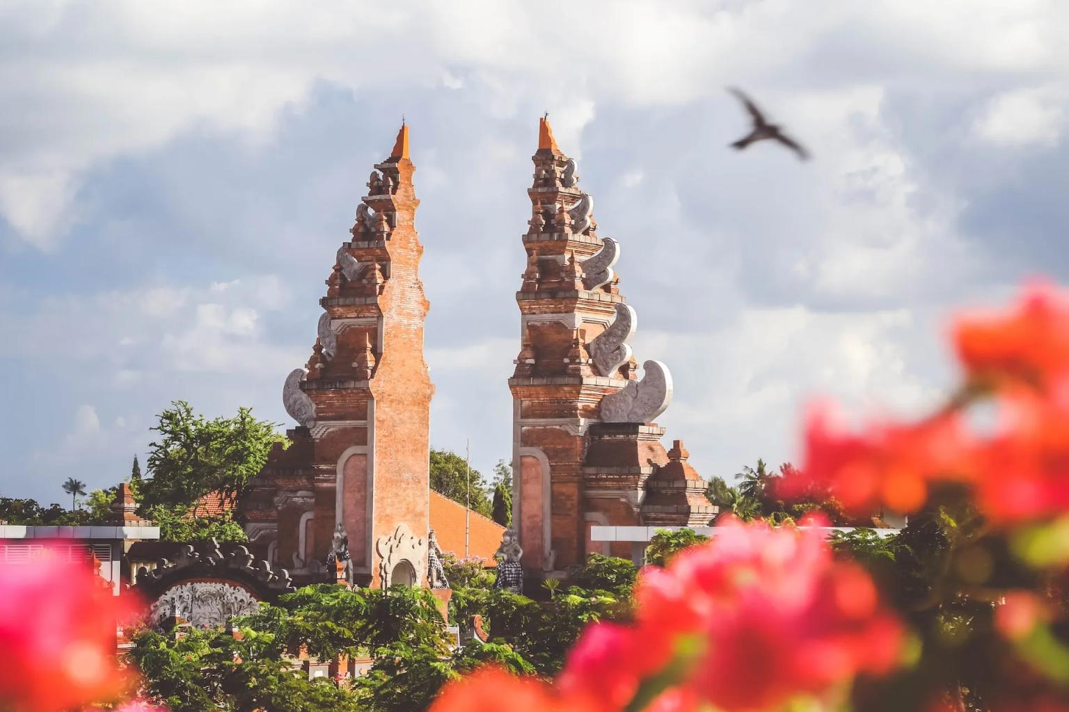 Balinese temple with ornate towers surrounded by greenery and colorful flowers.