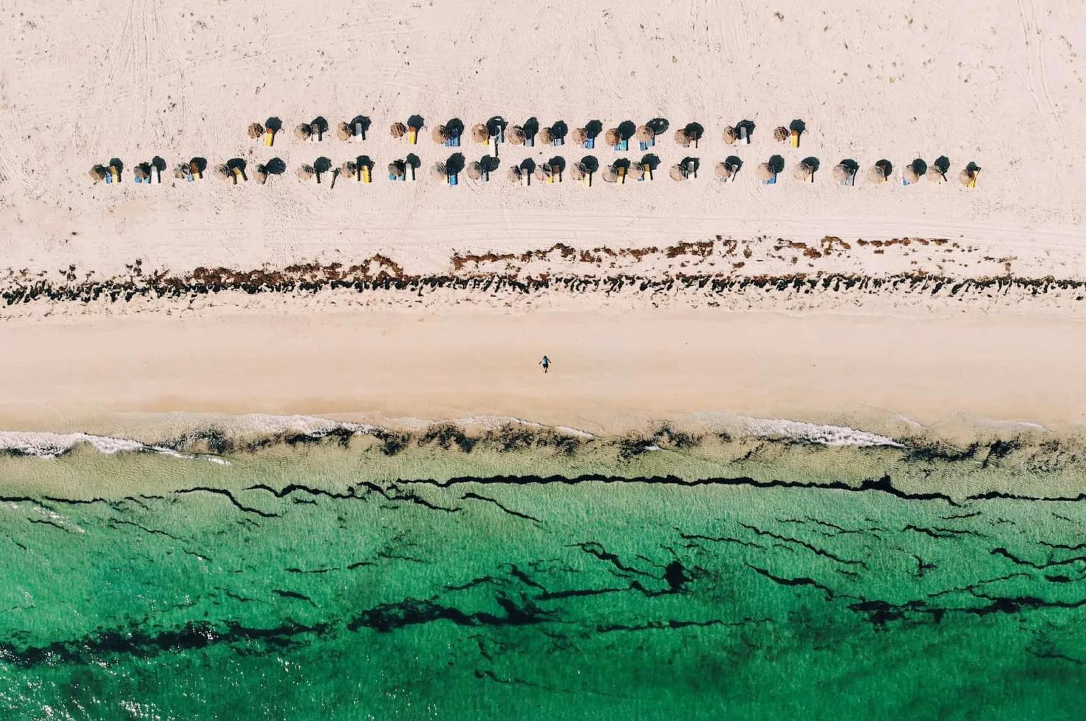 Praia de Djerba com guarda-sóis e mar verde-turquesa.