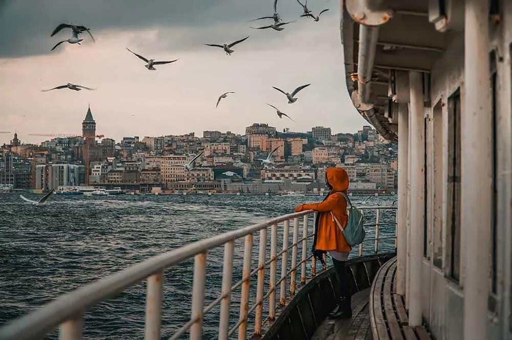 Pessoa em um barco, observando a cidade de Istambul e gaivotas voando.