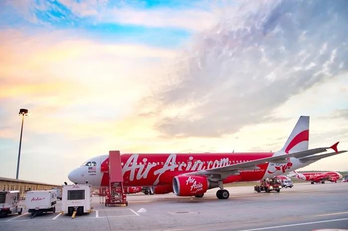 Avión de AirAsia en un aeropuerto bajo un cielo colorido al atardecer.