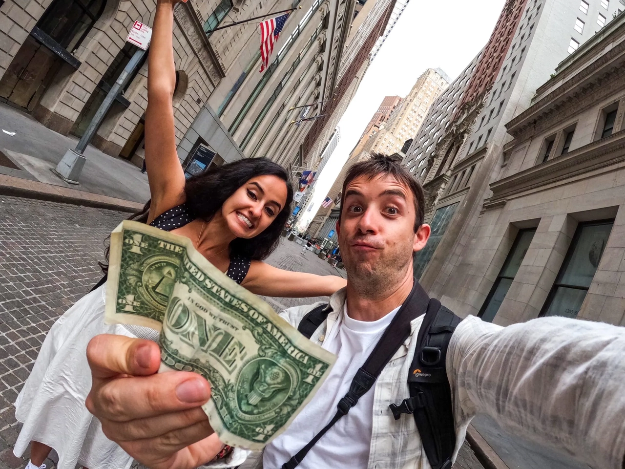 Pareja sonriente en la calle, mostrando un billete de un dólar.