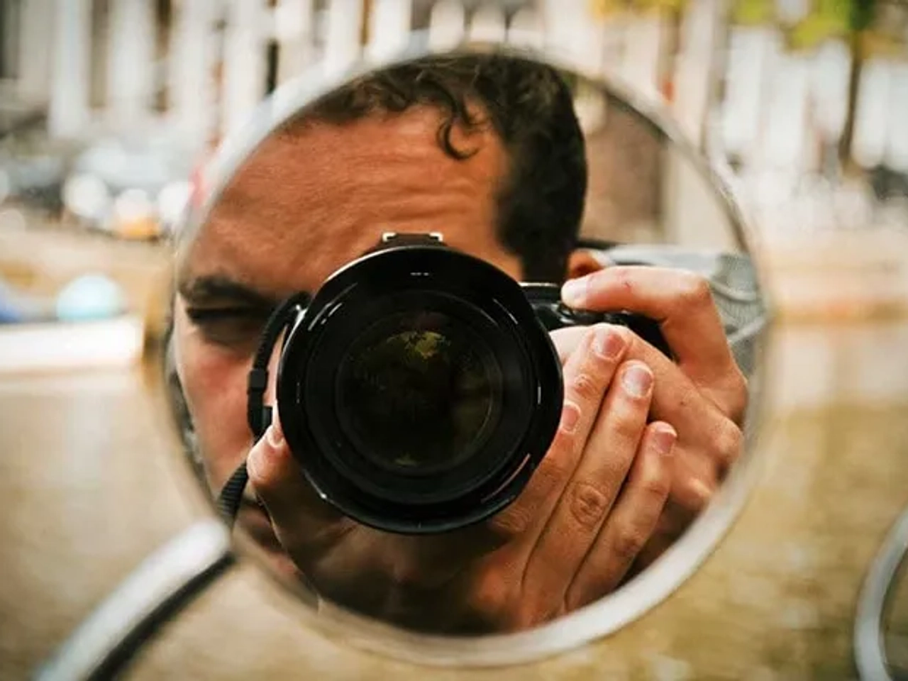 Fotógrafo reflejado en un espejo, sosteniendo una cámara en un entorno urbano.