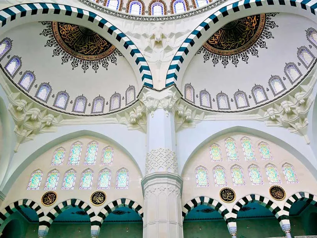 Interior de una mezquita con cúpulas decoradas y vitrales coloridos.