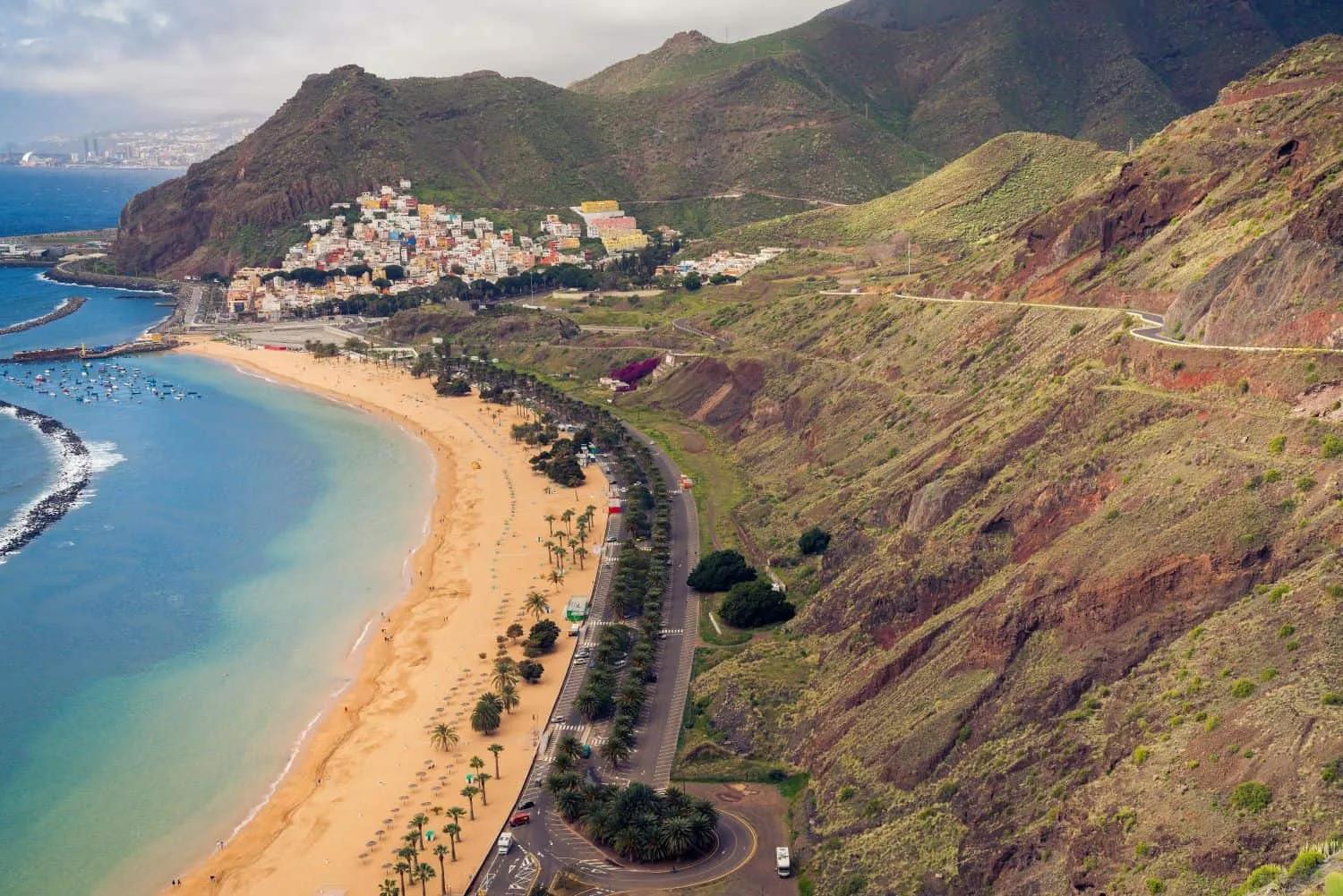Vista panorâmica de uma praia nas Ilhas Canárias, cercada por montanhas e cidade.