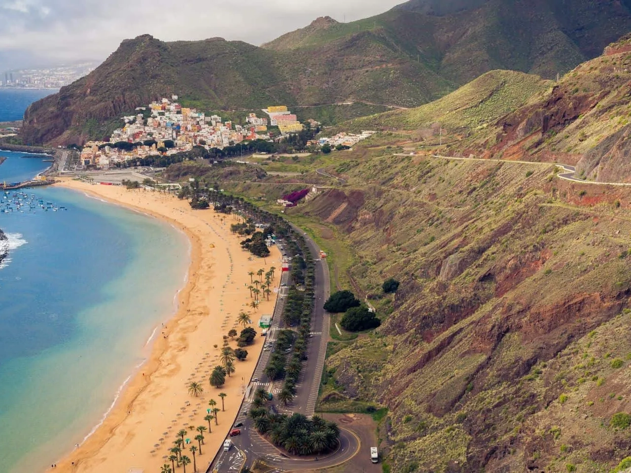 Vista panorâmica de uma praia nas Ilhas Canárias, cercada por montanhas e cidade.