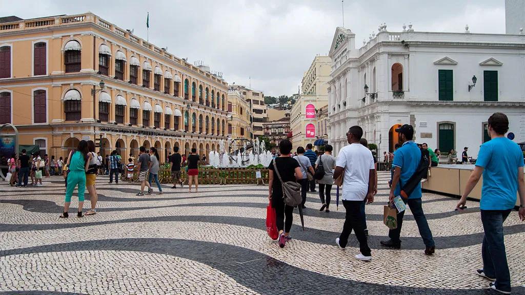 Pessoas caminhando em uma praça com edifícios históricos em Macau.