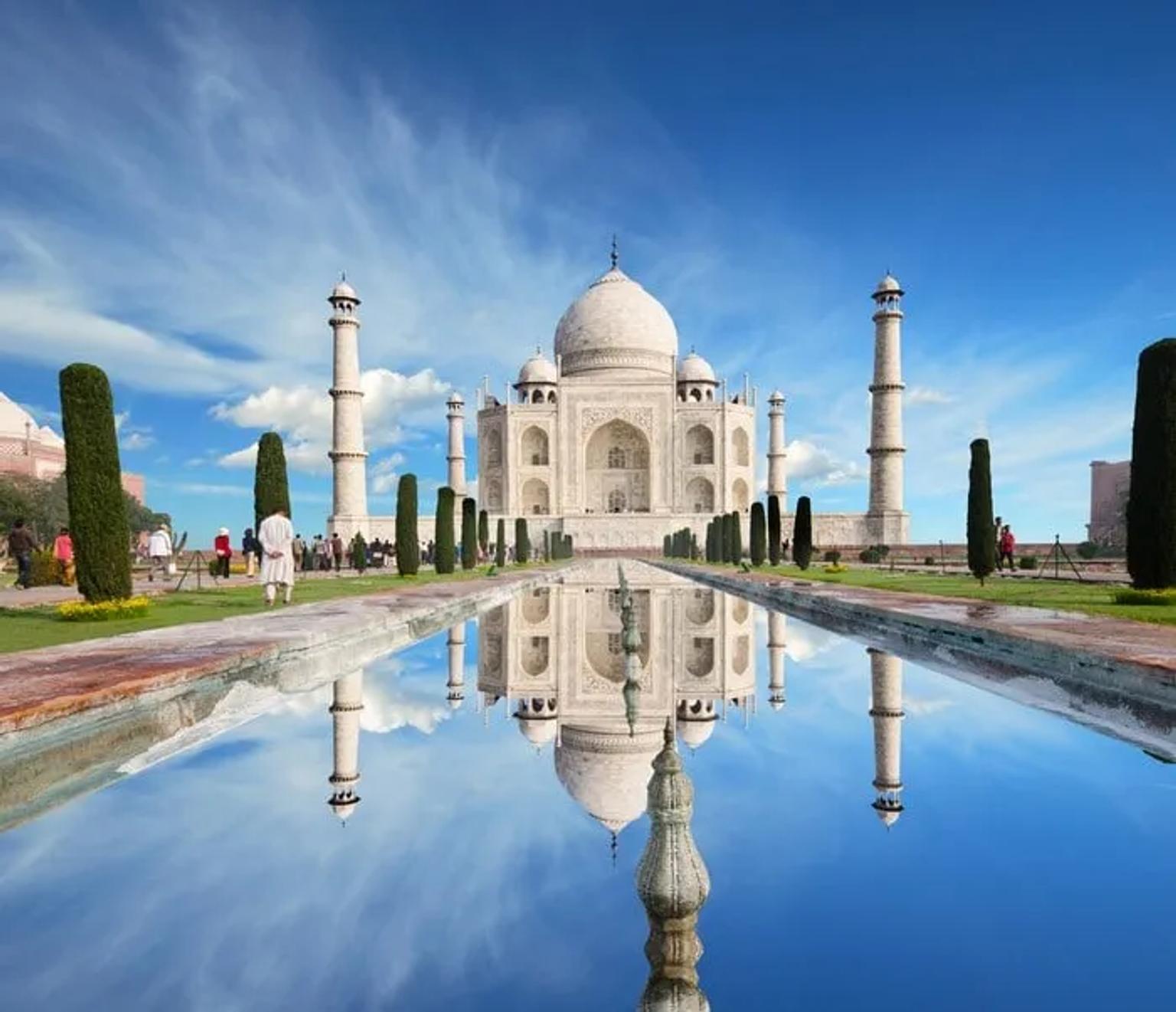 El Taj Mahal reflejado en un estanque, rodeado de jardines y visitantes.