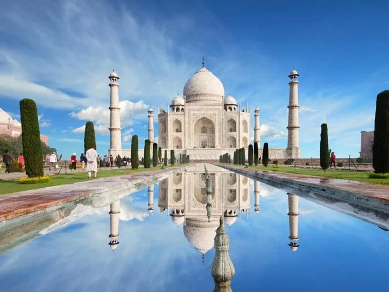 El Taj Mahal reflejado en un estanque, rodeado de jardines y visitantes.