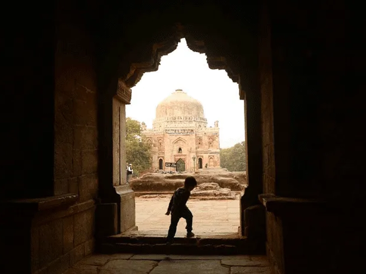 Niño caminando hacia un monumento histórico a través de un arco.