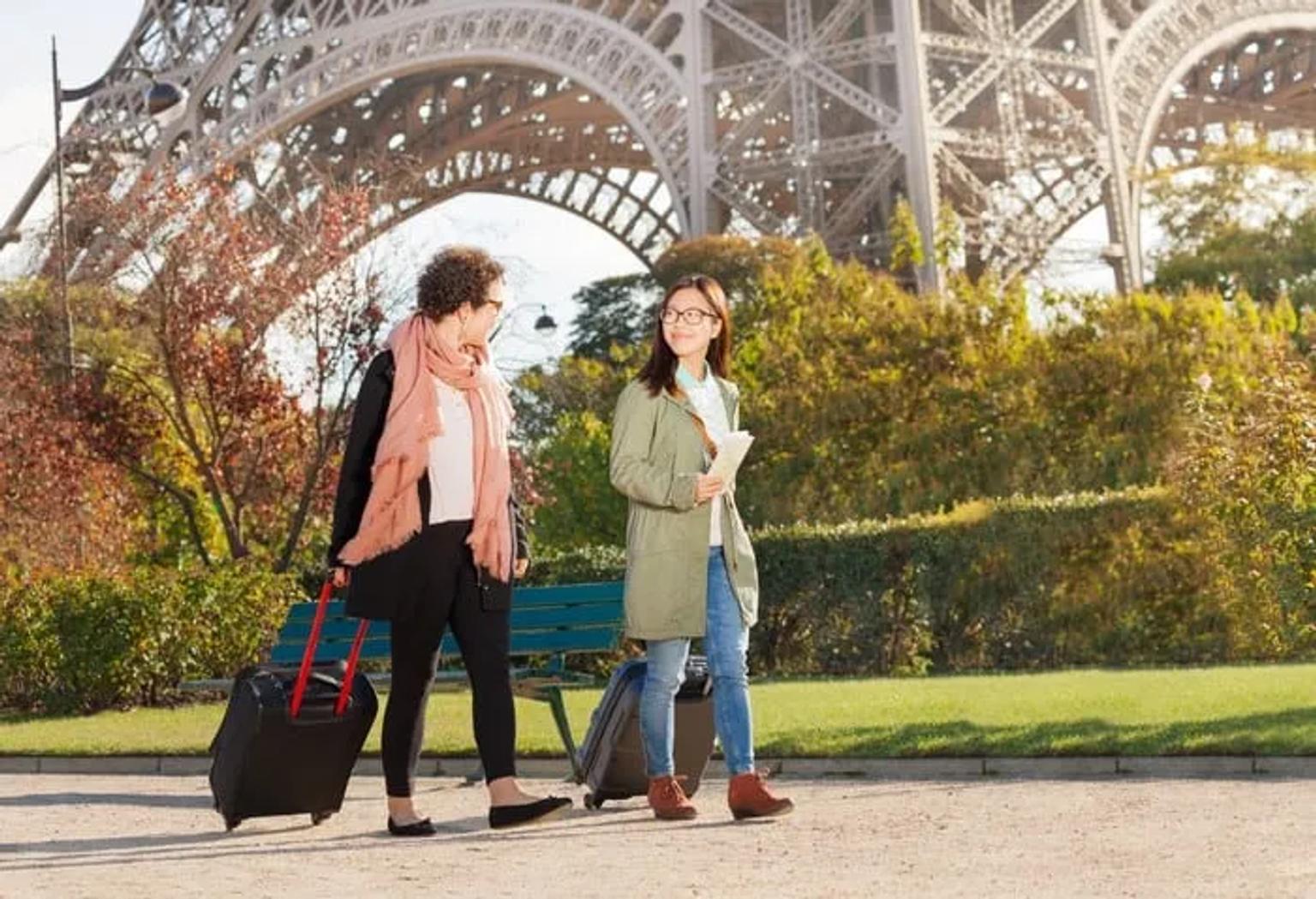 Dos mujeres caminando con maletas frente a la Torre Eiffel en París.
