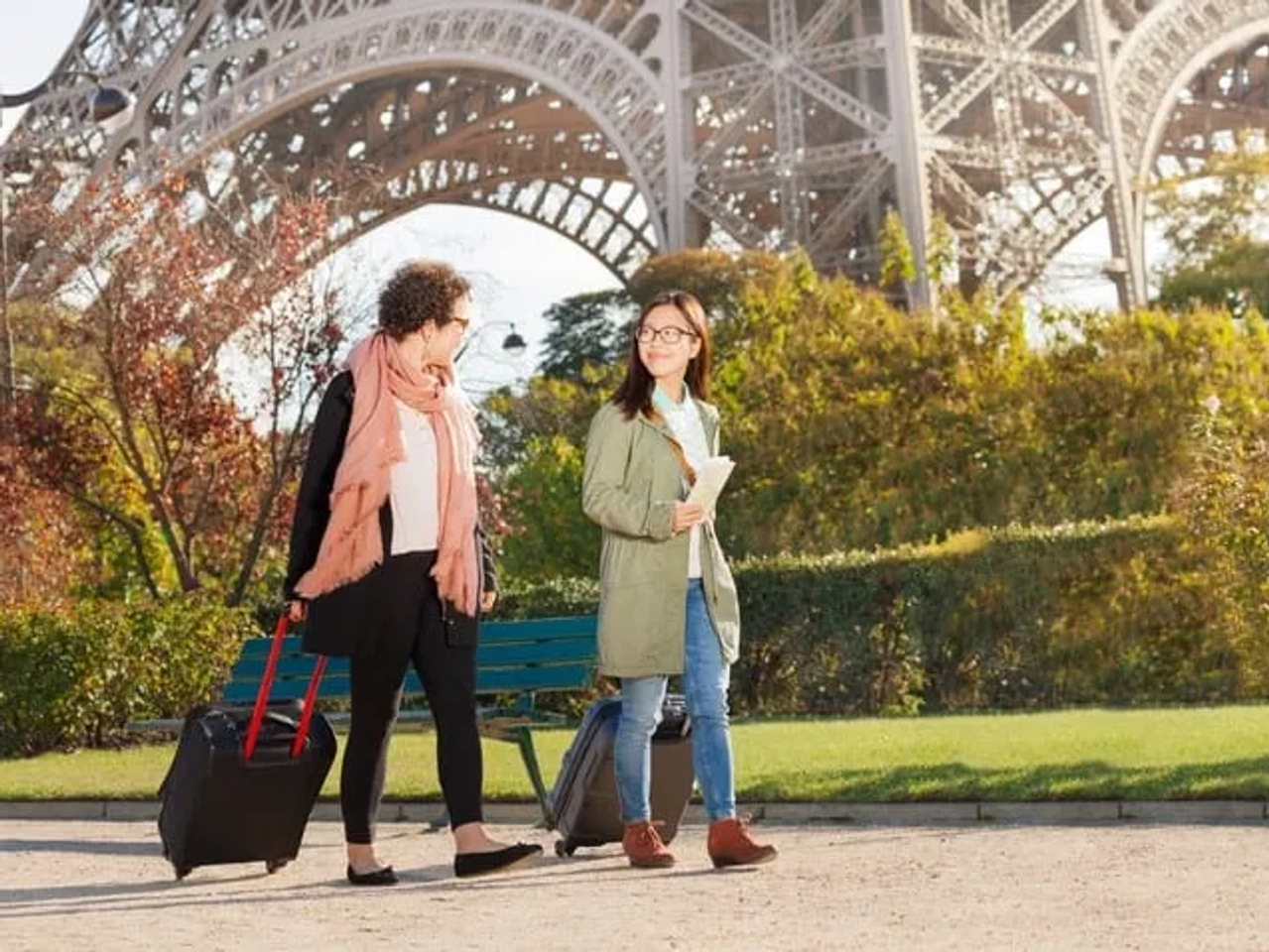 Dos mujeres caminando con maletas frente a la Torre Eiffel en París.