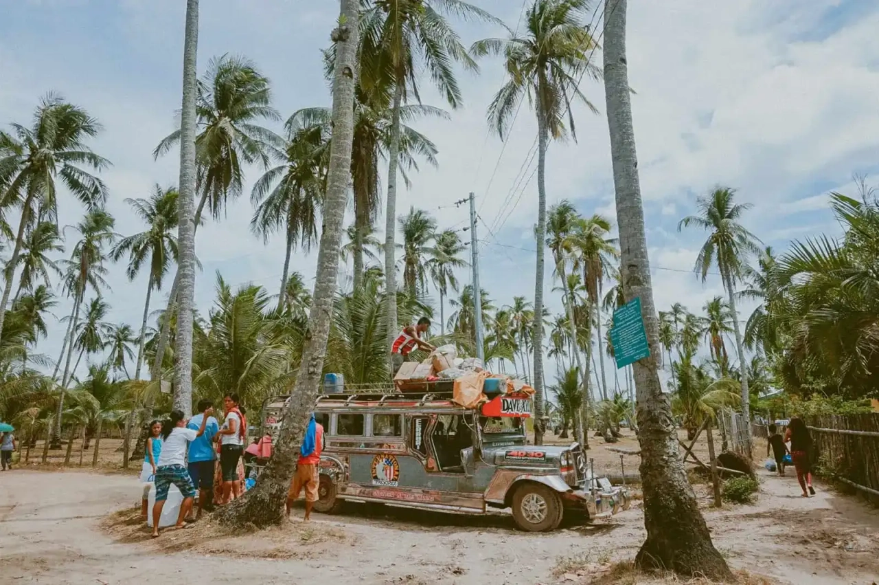 Grupo de personas junto a un jeepney en un paisaje tropical con palmeras.