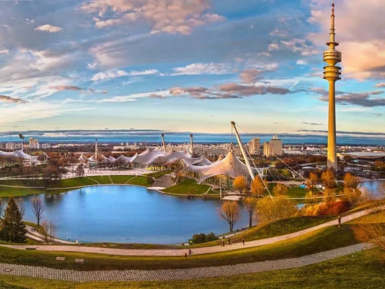 Vista panorâmica do Parque Olímpico de Munique, com lago e torres icônicas.