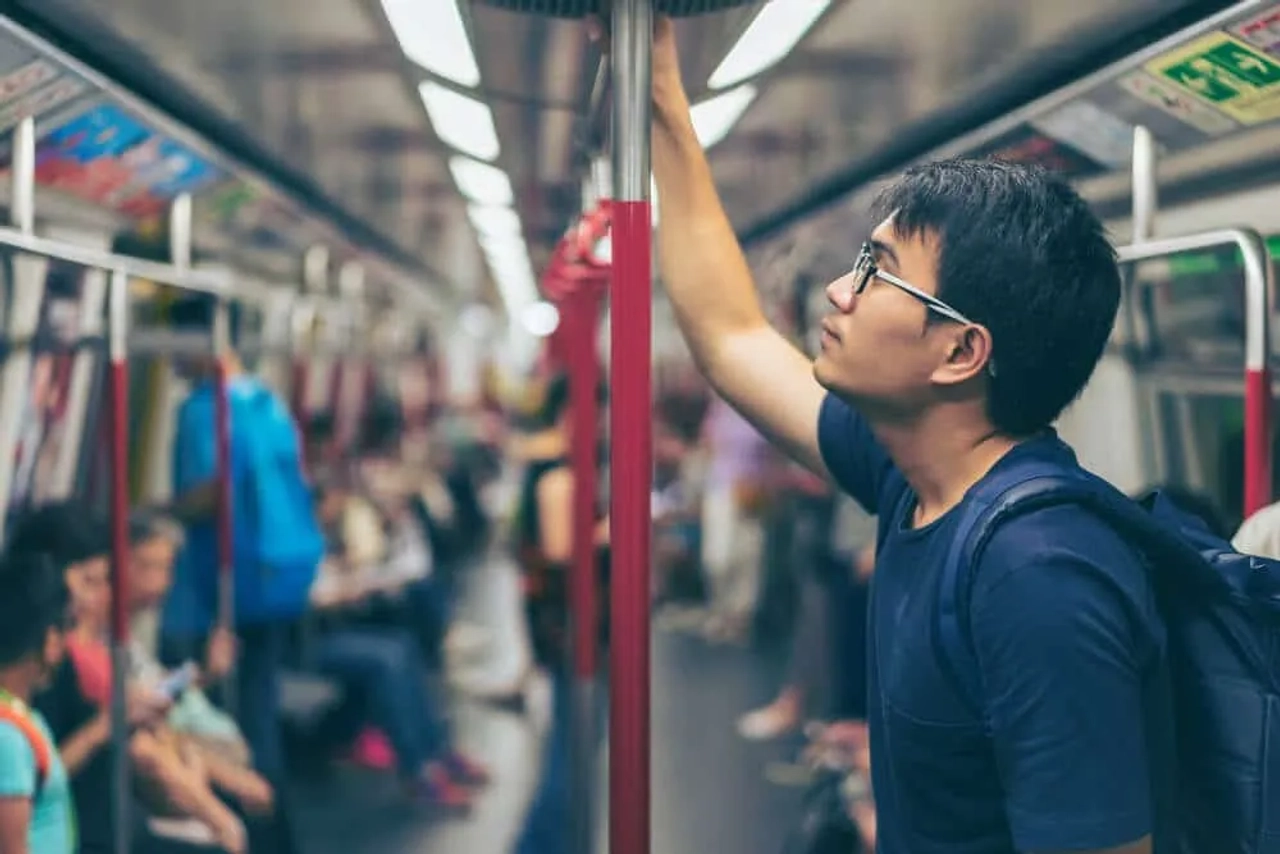rapaz com óculos azuis de pé num metro de hong kong
