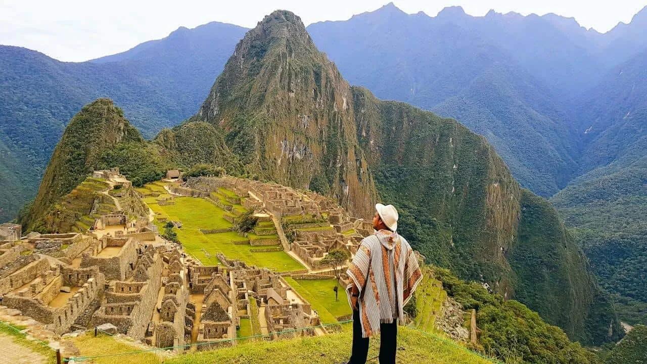 Vista panorâmica de Machu Picchu, com montanhas ao fundo e uma pessoa admirando.