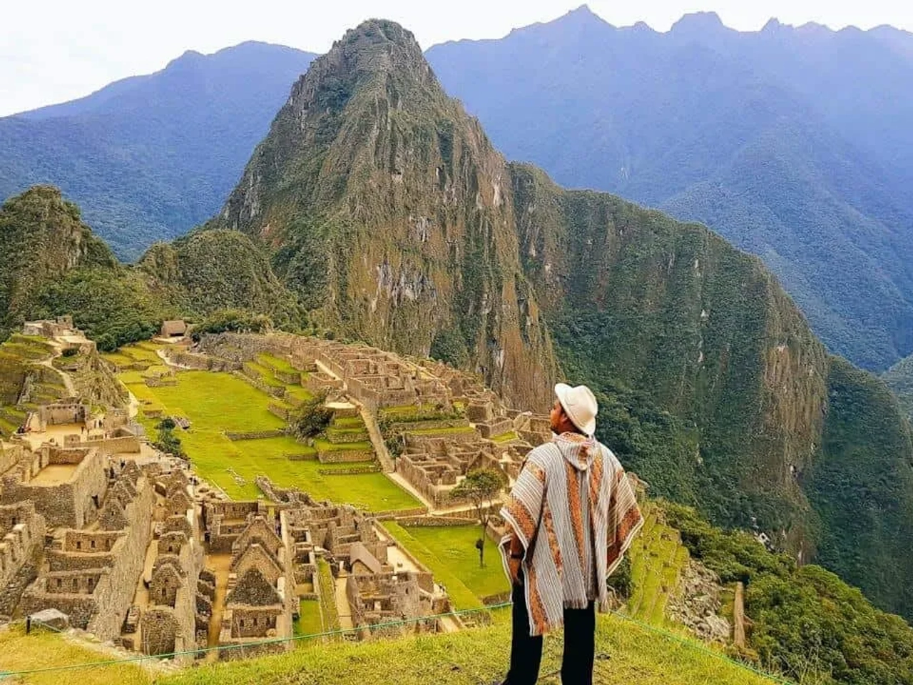 Vista panorâmica de Machu Picchu, com montanhas ao fundo e uma pessoa admirando.