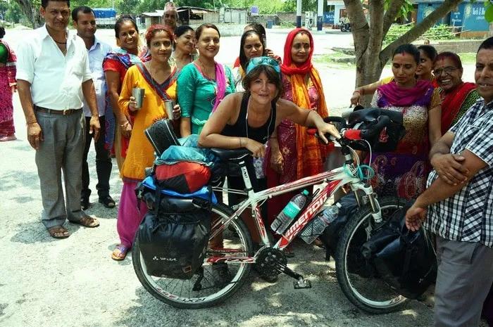 Mujer con bicicleta rodeada de un grupo de personas sonrientes en un entorno rural.