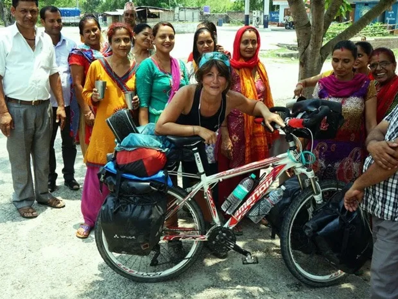 Mujer con bicicleta rodeada de un grupo de personas sonrientes en un entorno rural.
