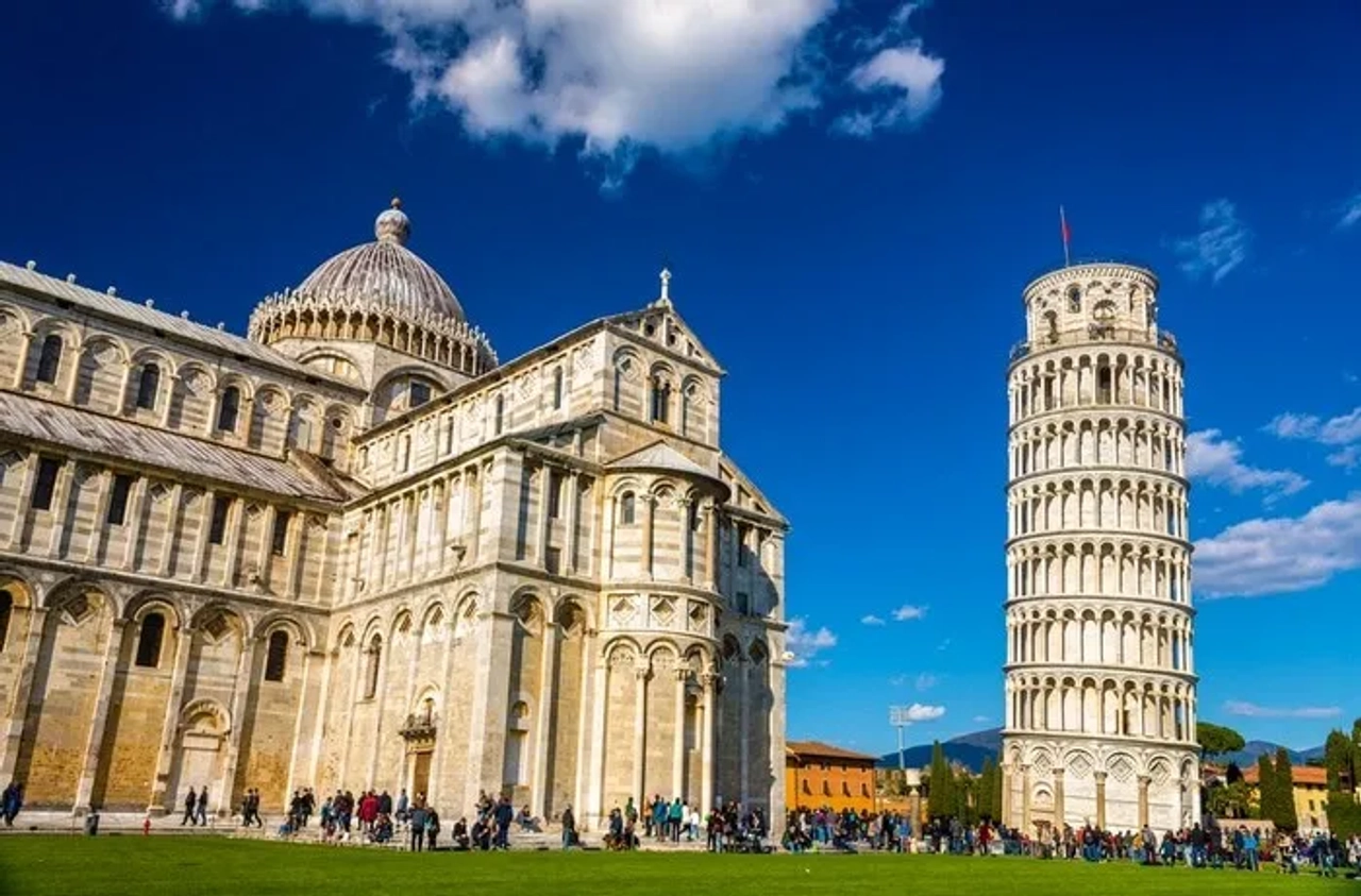 Torre de Pisa e catedral na Piazza dei Miracoli, em Itália, com céu azul.