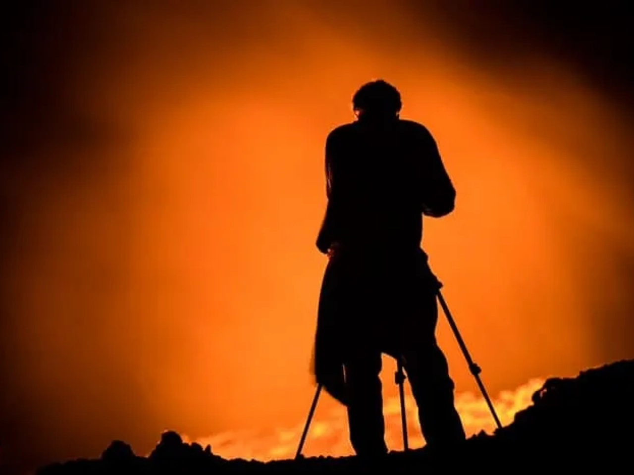 Silueta de un fotógrafo frente a un paisaje ardiente y luminoso.