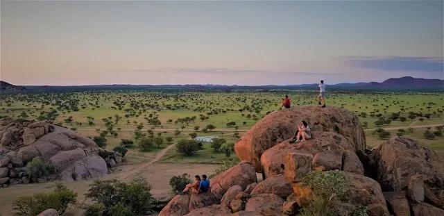 pessoas sentadas numa rocha com vista para arvores verdes na namibia