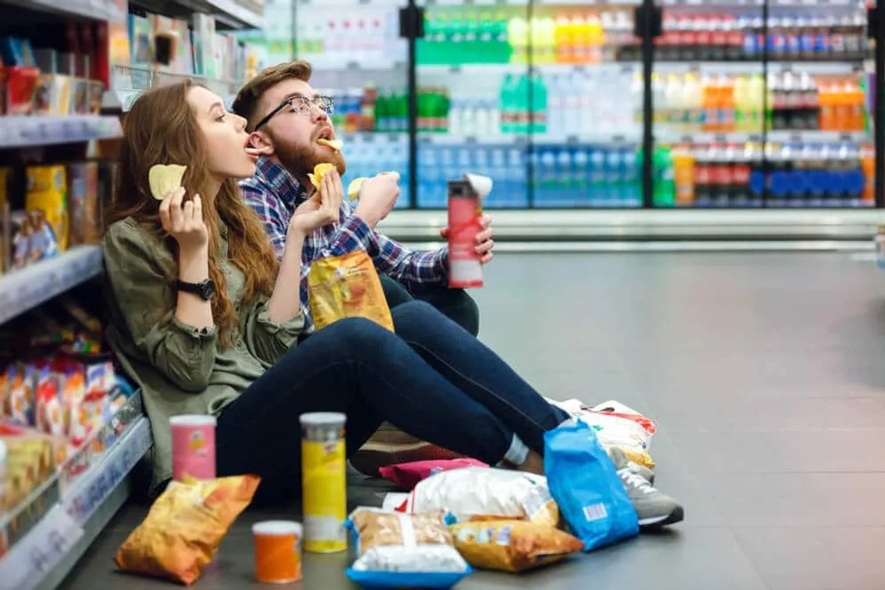 dois jovens comem batatas fritas no corredor de um supermercado