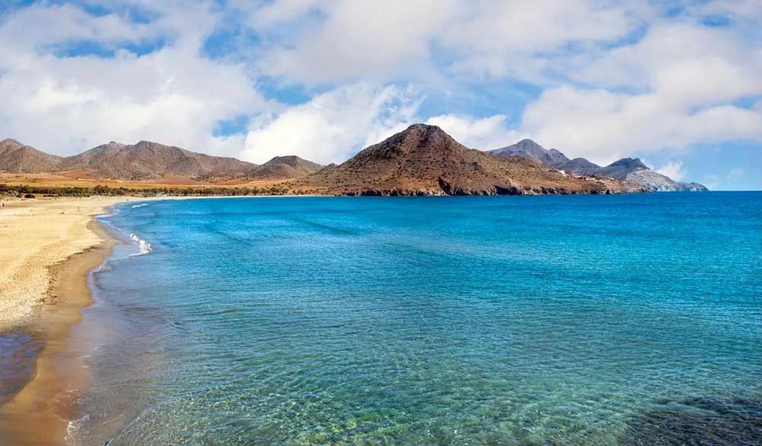 Playa con aguas cristalinas y montañas al fondo, ideal para viajar en España.