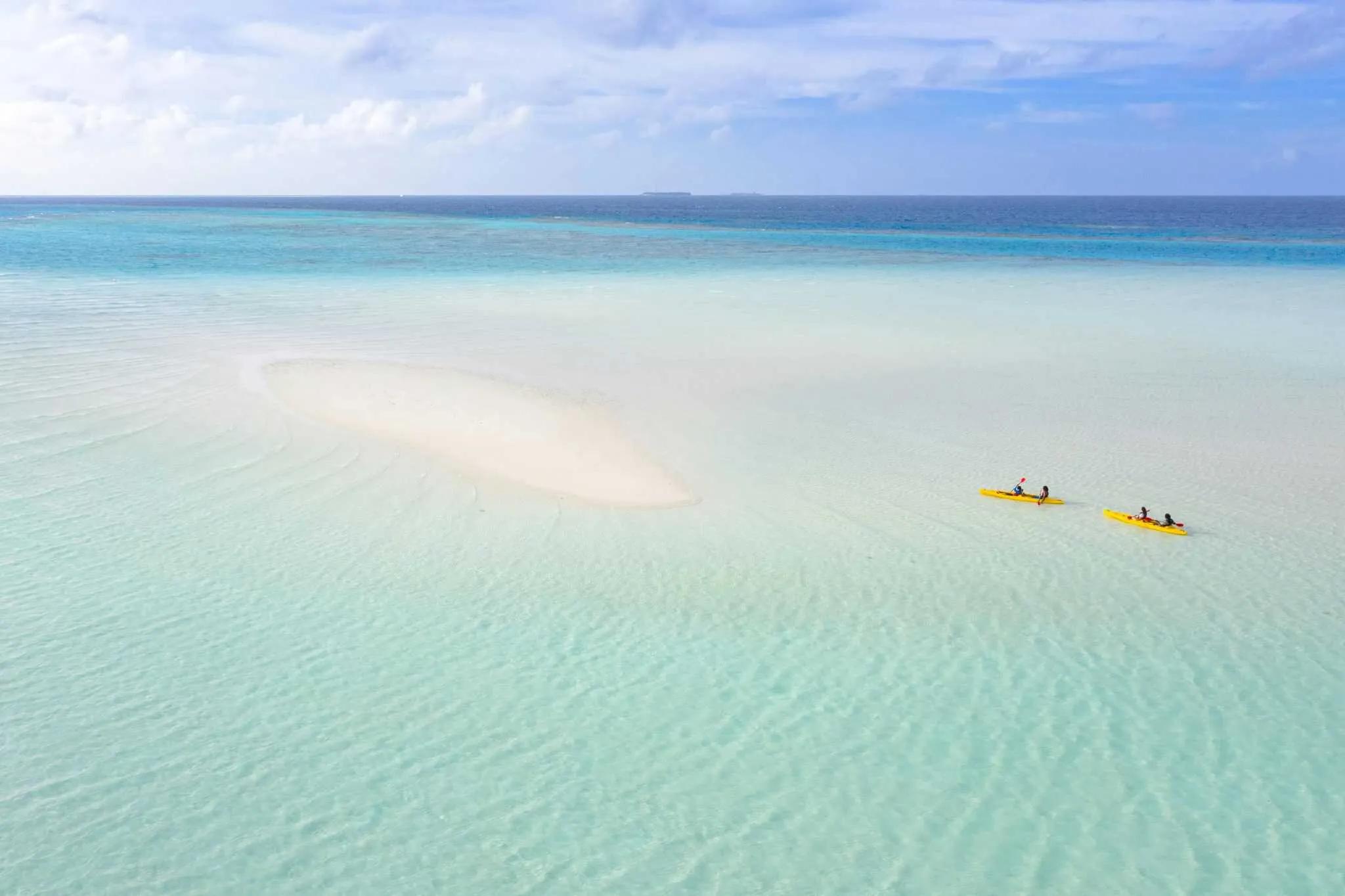 Dos kayaks amarillos navegan en aguas turquesas cerca de una isla de arena.