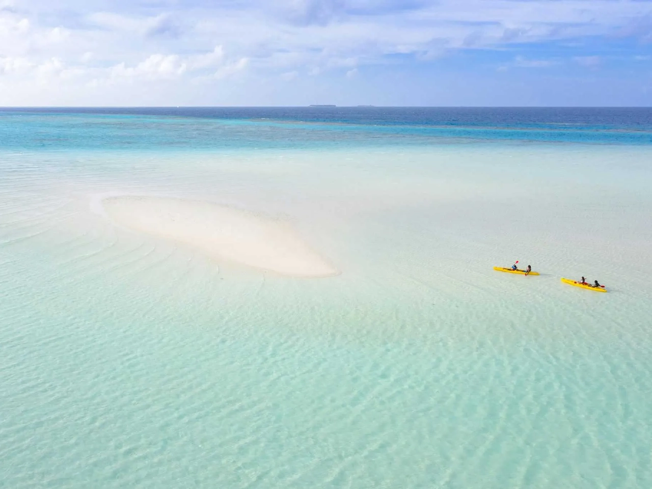 Dos kayaks amarillos navegan en aguas turquesas cerca de una isla de arena.