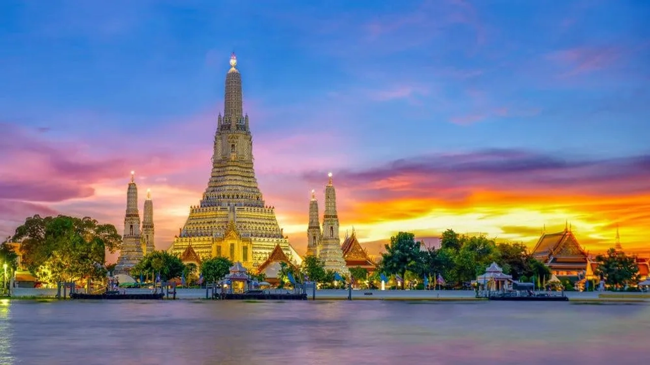 Wat Arun illuminato al tramonto a Bangkok, visto dal fiume Chao Phraya, con cielo colorato e templi thailandesi sulla riva.
