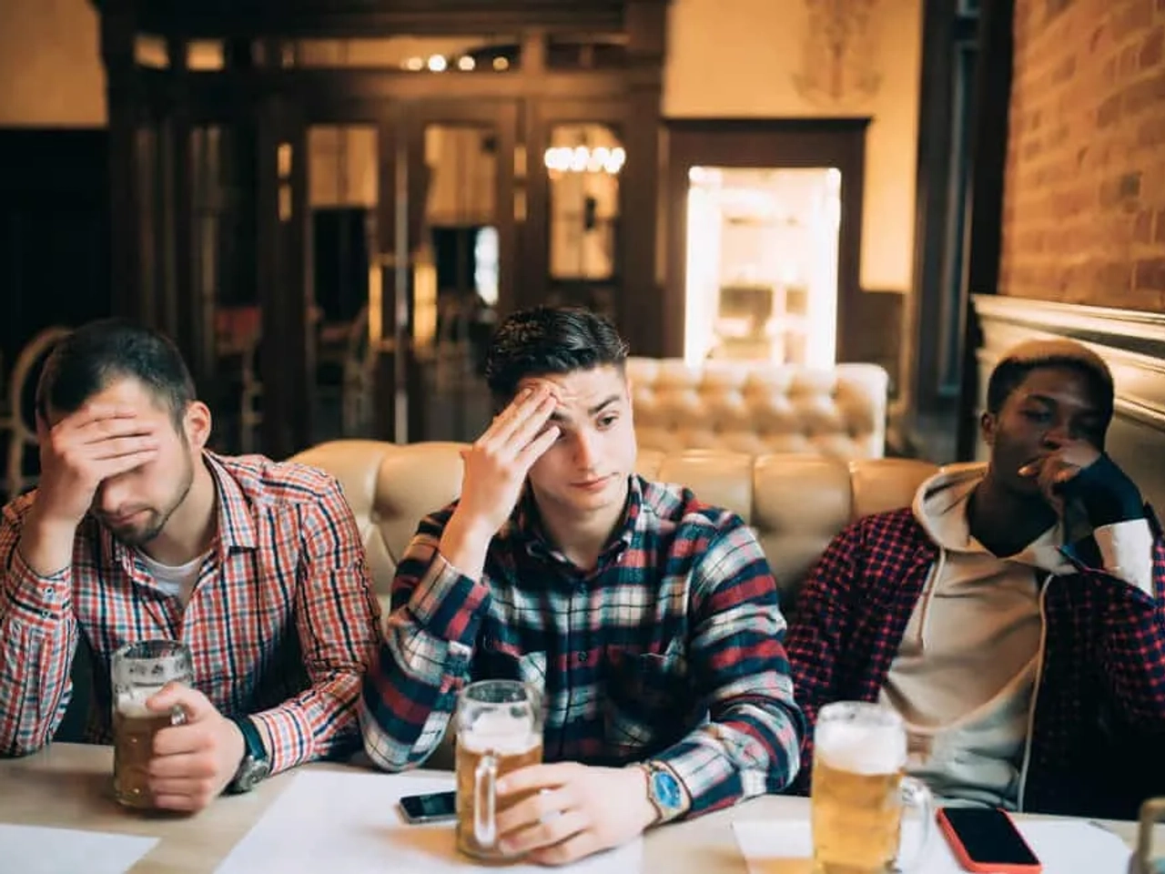 tres amigos chateados num bar com cervejas