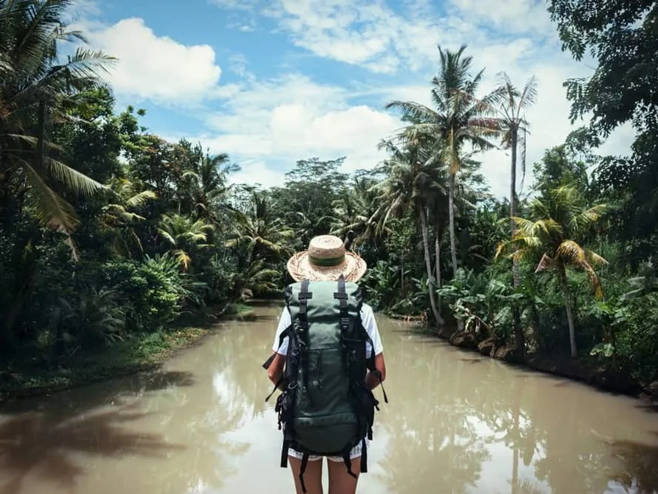 Persona con mochila frente a un río rodeado de vegetación tropical.