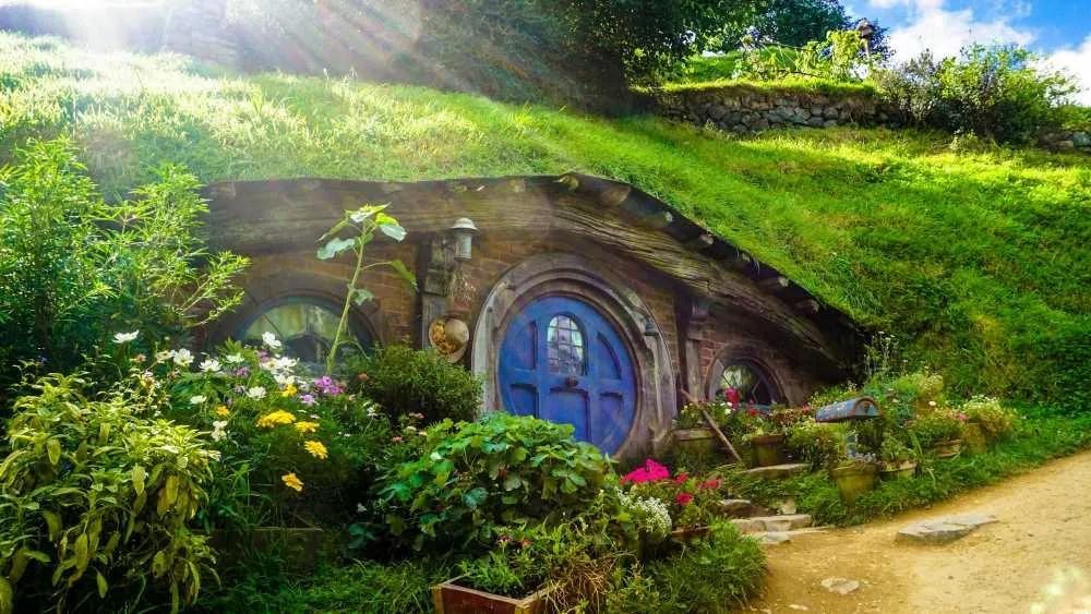 Casa hobbit rodeada de flores y vegetación en un paisaje natural.