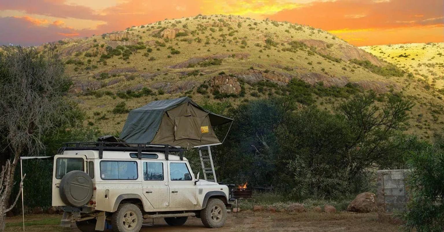 Vehículo todoterreno con tienda de campaña en un paisaje montañoso al atardecer.