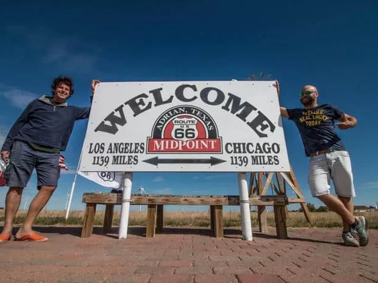 Dos hombres posan junto a un cartel que marca el punto medio de la Ruta 66.
