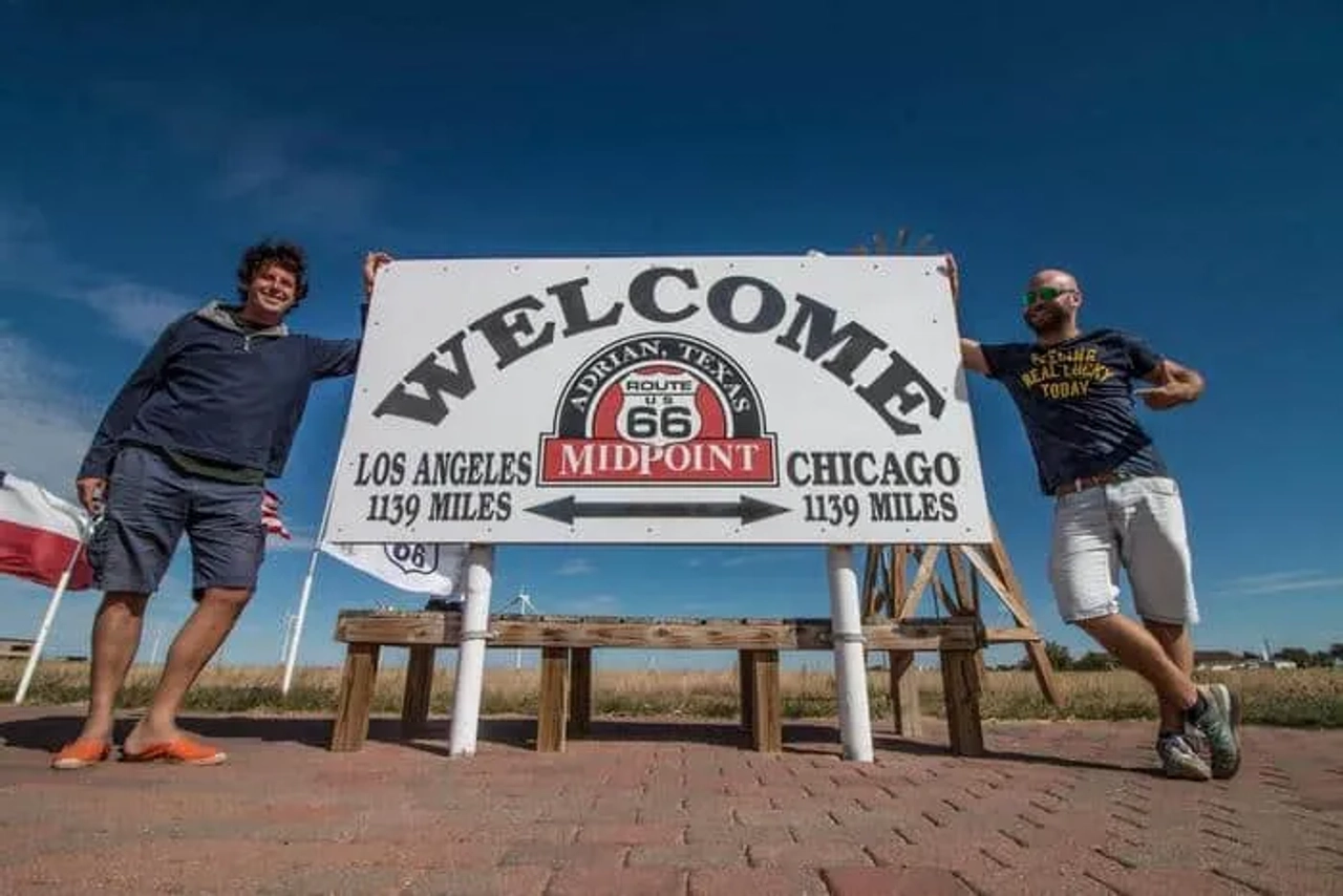 Dos hombres posan junto a un cartel que marca el punto medio de la Ruta 66.