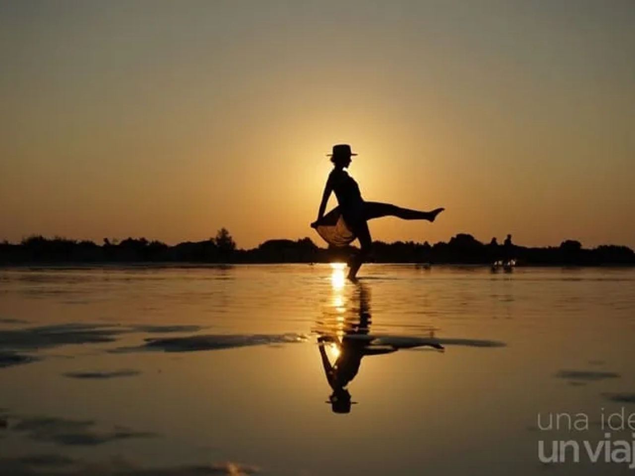 Silueta de mujer bailando al atardecer, reflejada en el agua.