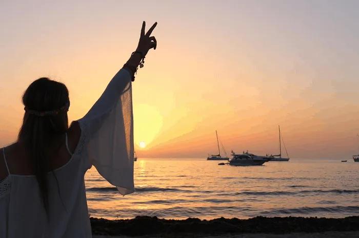 Persona disfrutando de un atardecer en la playa, con barcos en el fondo.