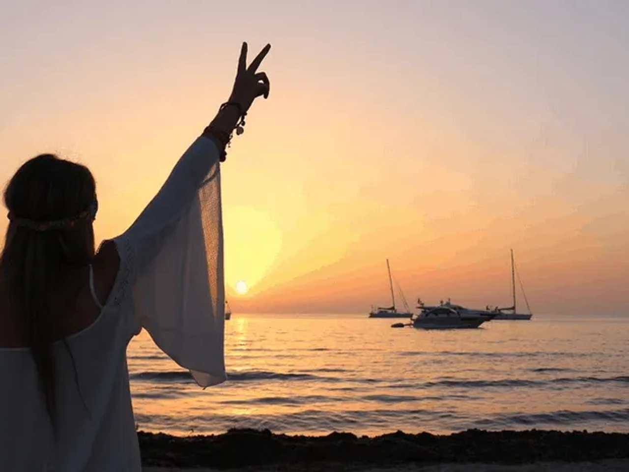 Persona disfrutando de un atardecer en la playa, con barcos en el fondo.