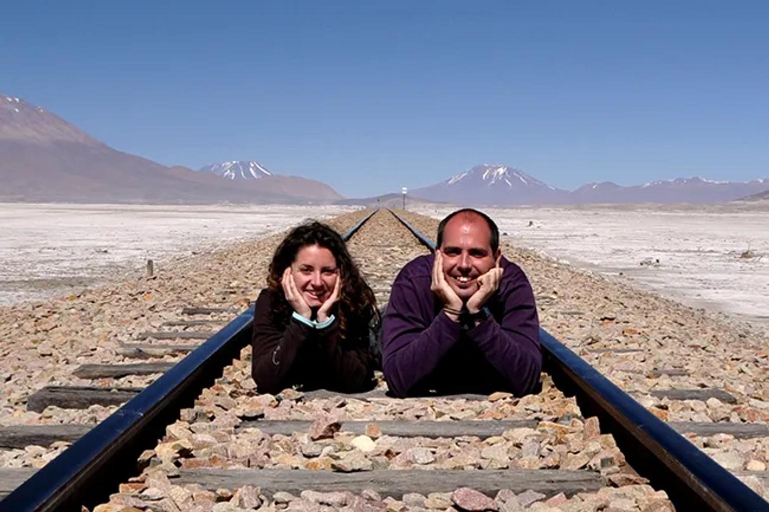 Celia y Enric posan sobre rieles en un paisaje desértico montañoso.