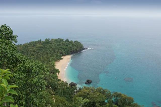 Praia isolada em São Tomé e Príncipe, cercada por vegetação e águas cristalinas.