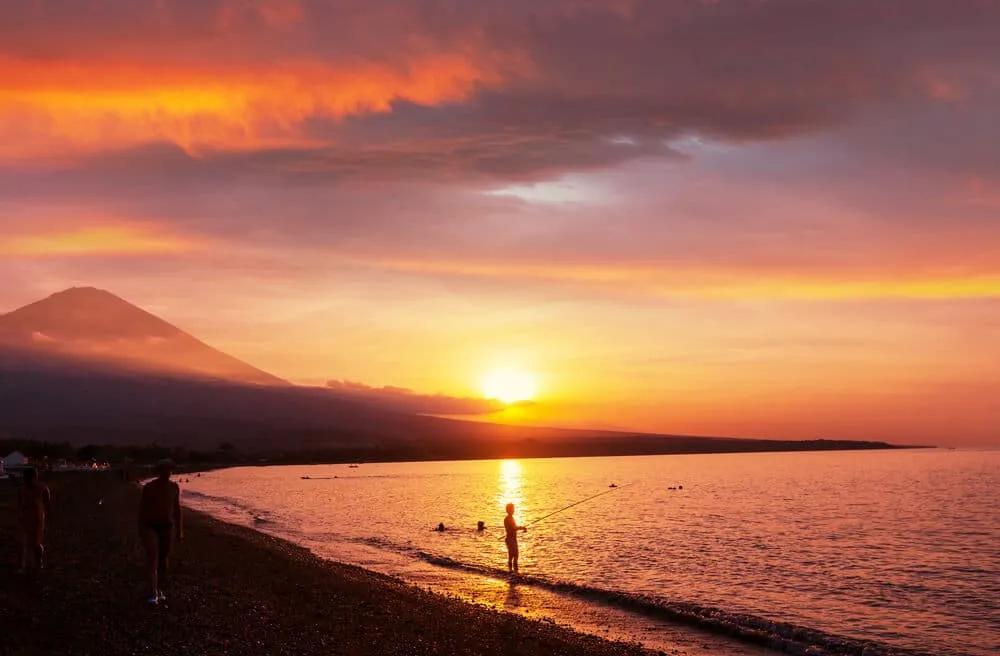 pessoa a pescar na praia de amed e vulcao agung ao por do sol
