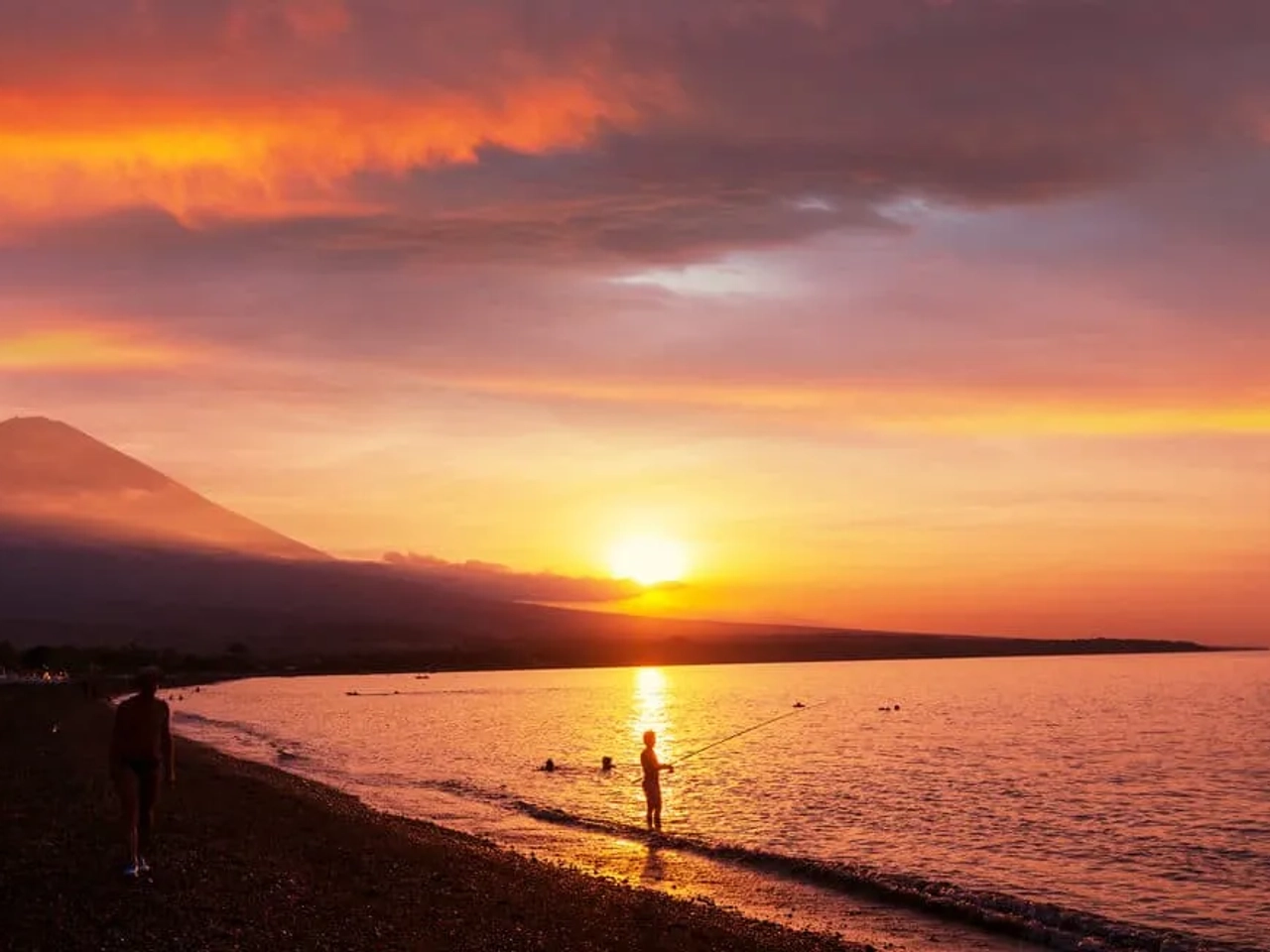 pessoa a pescar na praia de amed e vulcao agung ao por do sol