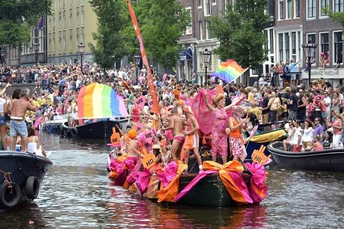 Desfile del Día del Orgullo Gay en un canal, con barcos decorados y multitudes celebrando.