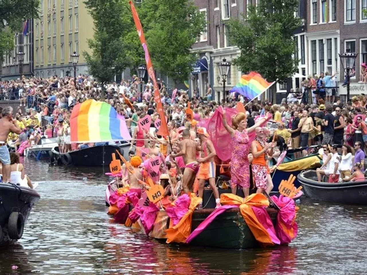 Desfile del Día del Orgullo Gay en un canal, con barcos decorados y multitudes celebrando.