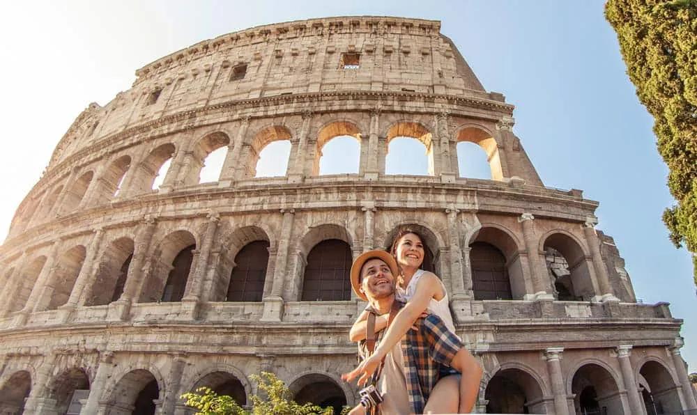 Pareja sonriente frente al Coliseo en Roma, disfrutando de su viaje.