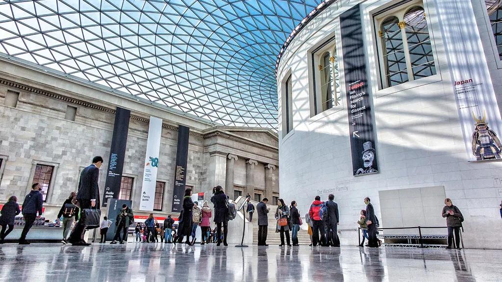Interior do Museu Britânico, com visitantes e teto de vidro impressionante.
