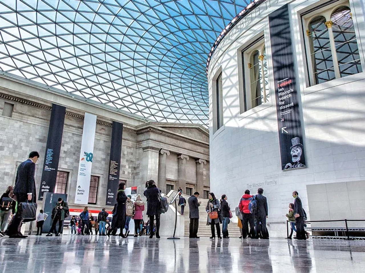 Interior do Museu Britânico, com visitantes e teto de vidro impressionante.